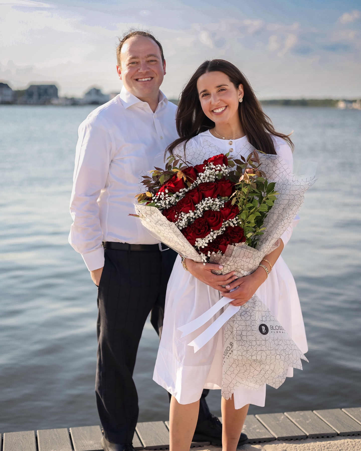 An engaged couple with a bouquet by the water
